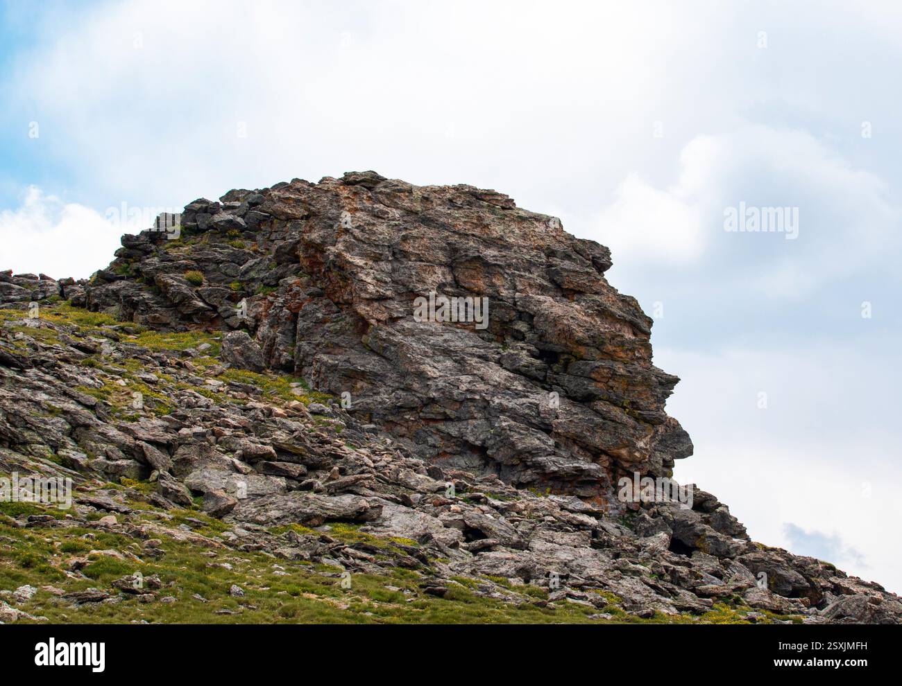 A large rock formation stands prominently on a grassy slope, with ...