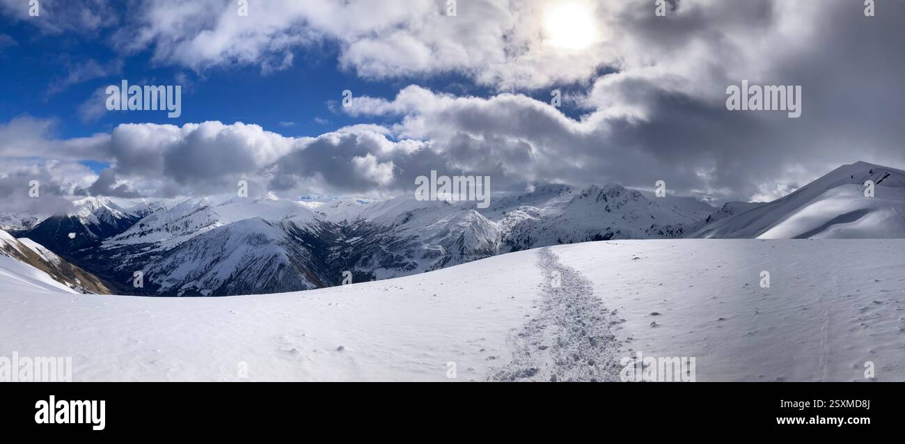 Footprints in pristine snow lead to majestic alpine peaks under a shifting sky, capturing the serenity and adventure of a breathtaking winter journey. - Smartphone Captured Stock Image