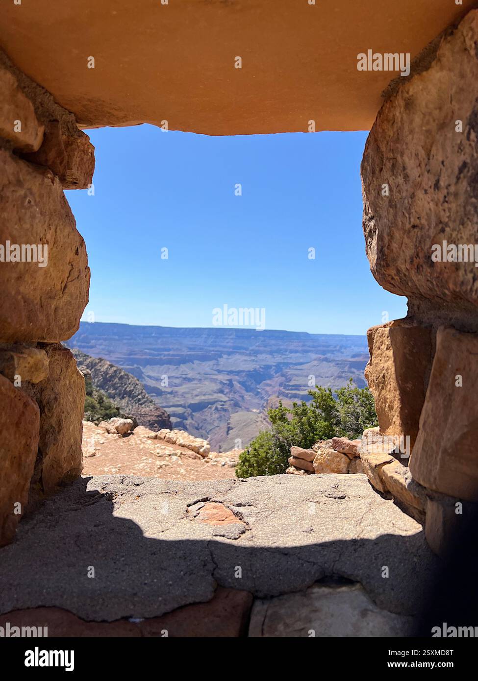 A natural rock window at Desert View frames a stunning Grand Canyon vista, where warm sunlit tones contrast with the deep blue sky and rugged depths. - Smartphone Captured Stock Image