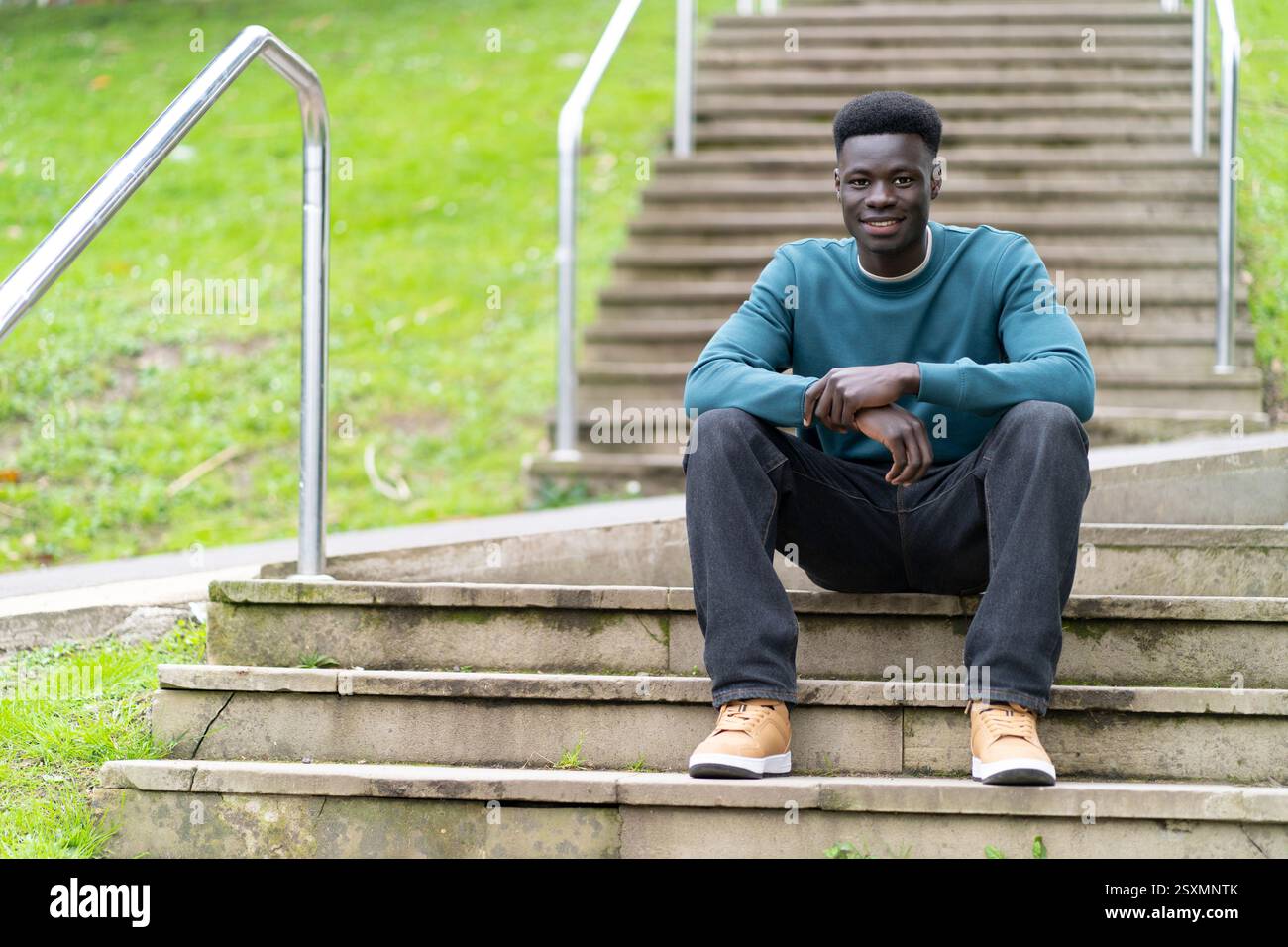 Portrait of a young black man sitting on some stairs in a university ...
