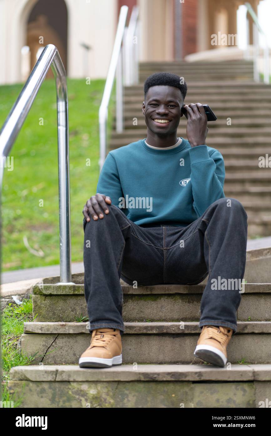 Happy student using his smartphone while sitting on some steps in a university campus Stock Photo