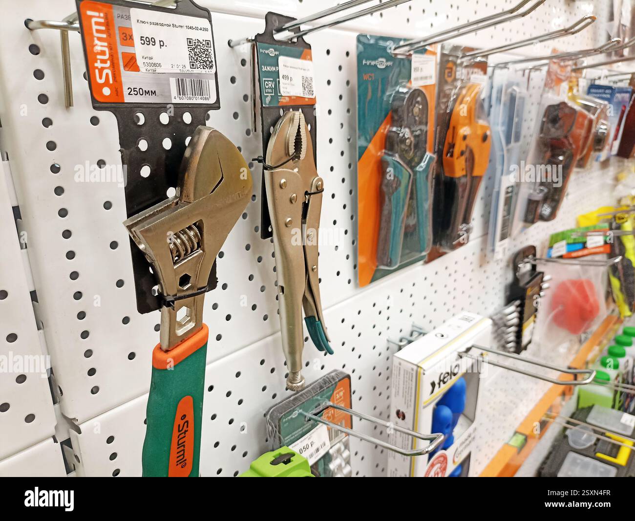 Assorted hand tools displayed on pegboard in hardware store aisle. Stock Photo