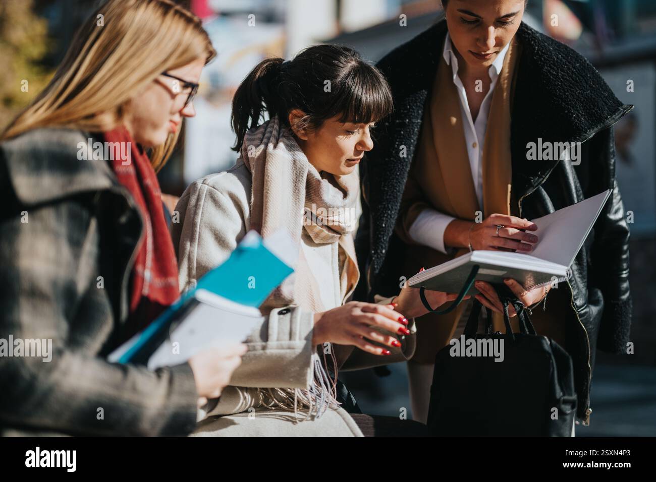 Three multicultural businesswomen collaborating outdoors with documents and notes Stock Photo