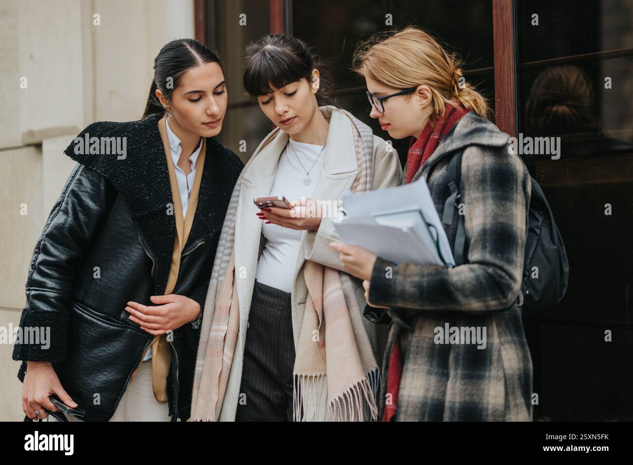 Three professional women collaborating and using smart phone outdoors Stock Photo