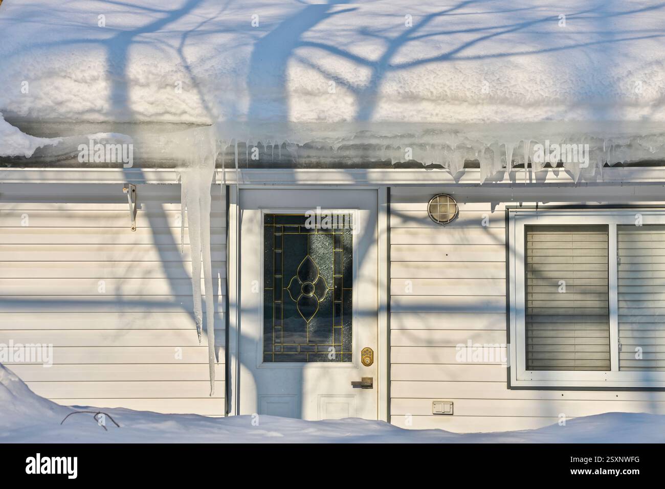 Large icicles and ice dams form at the edge of the snow-covered roof ...