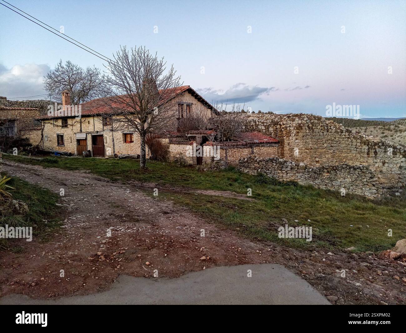 European Medieval Rural Area A rustic stone house with wooden doors and a red-tiled roof, next to ...