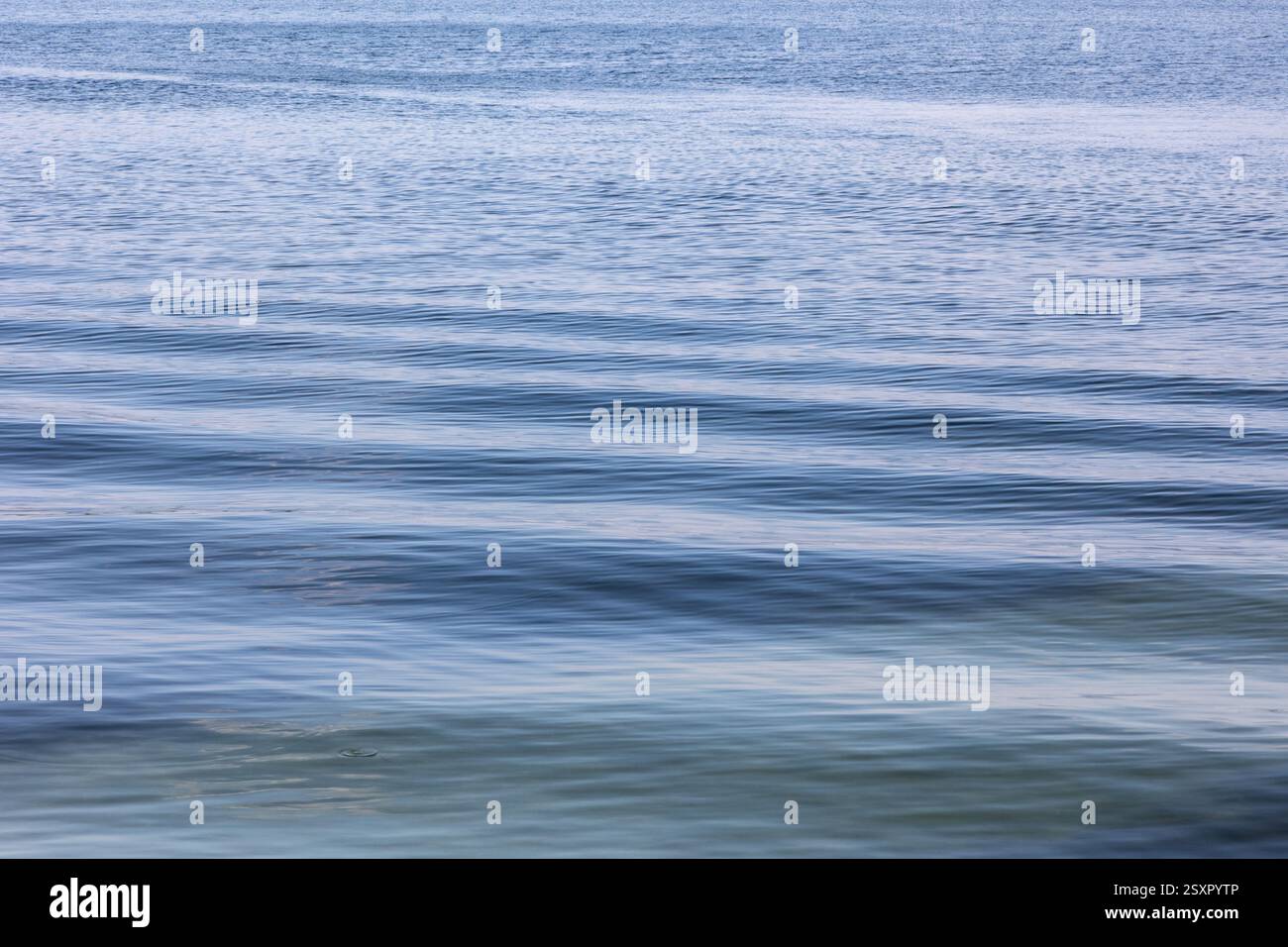 Slowly moving littles waves on water with reflections of the blue sky ...