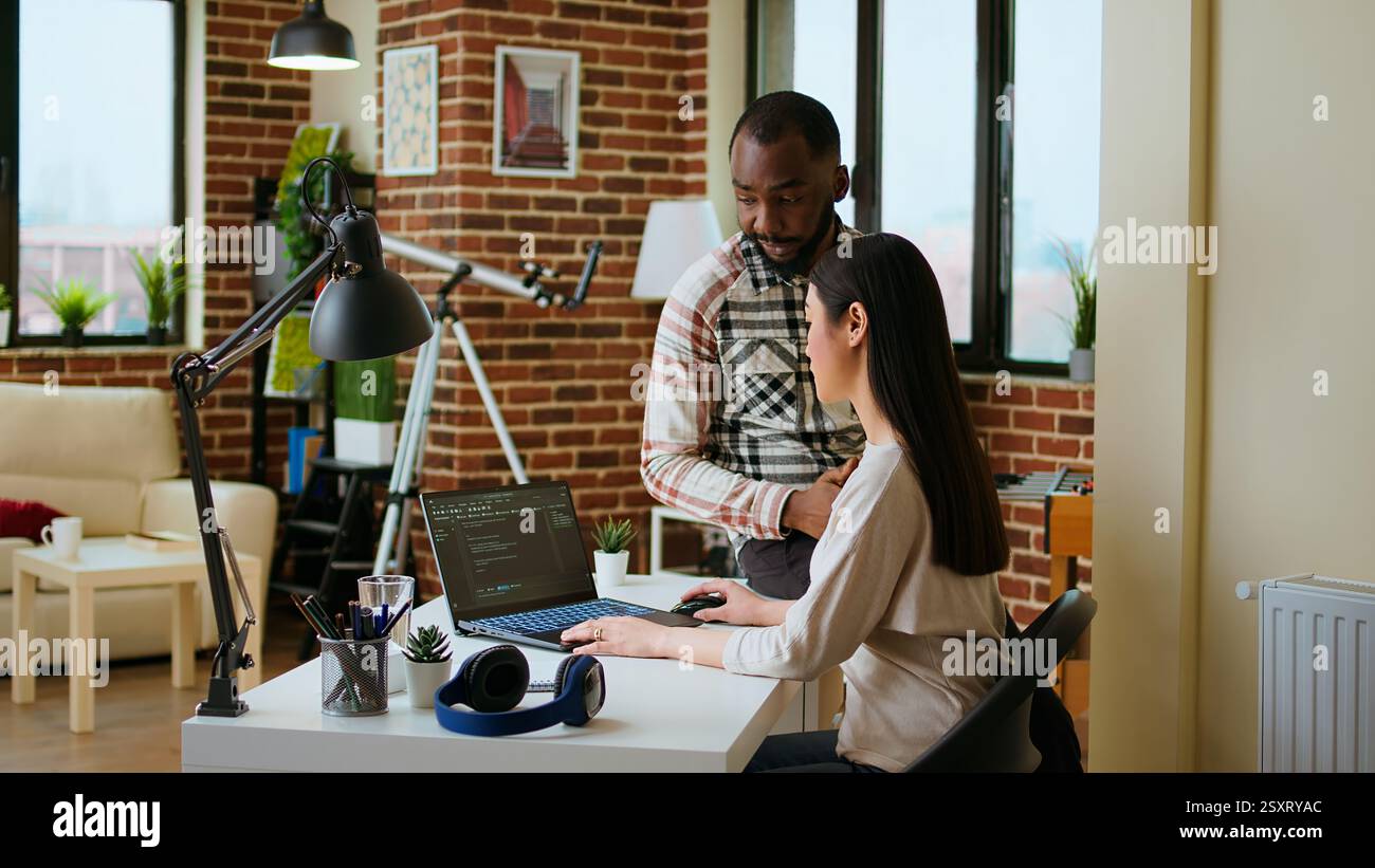 Interracial creative team programing code on a laptop and debugging, using digital tools at home. Professional coders team working on software development and internet security. Camera A. Stock Photo