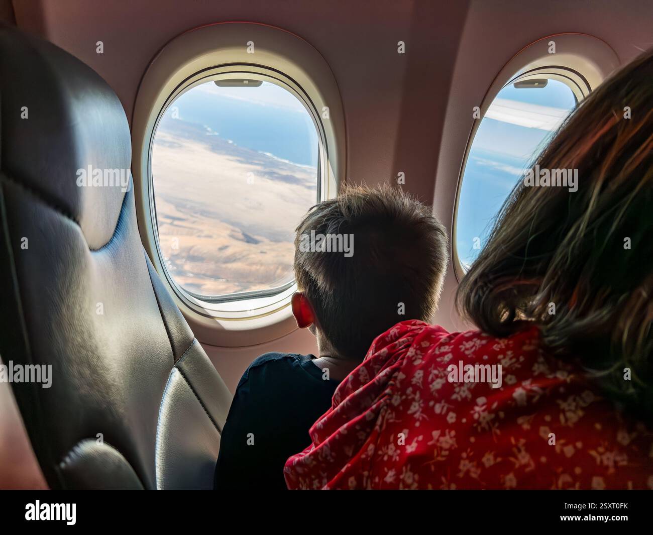 Child gazing out the airplane window at the scenic landscape during daytime flight with an adult sitting nearby - Smartphone Captured Stock Image