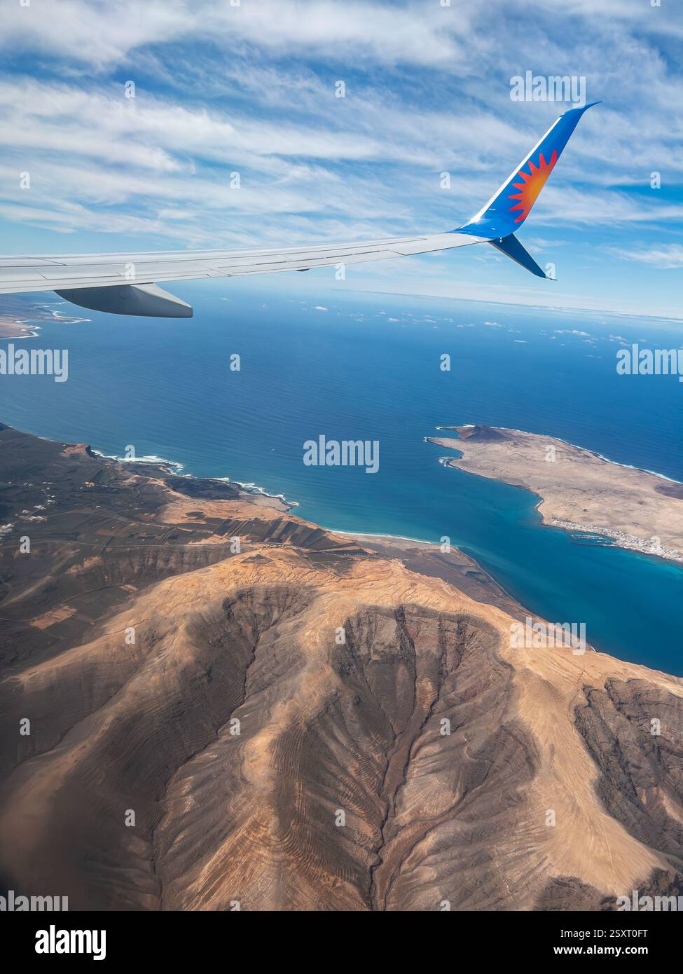 Aerial view of rugged coastline and ocean from airplane window with wing visible under a partly cloudy sky over Lanzarote Jet2 airlines - Smartphone Captured Stock Image