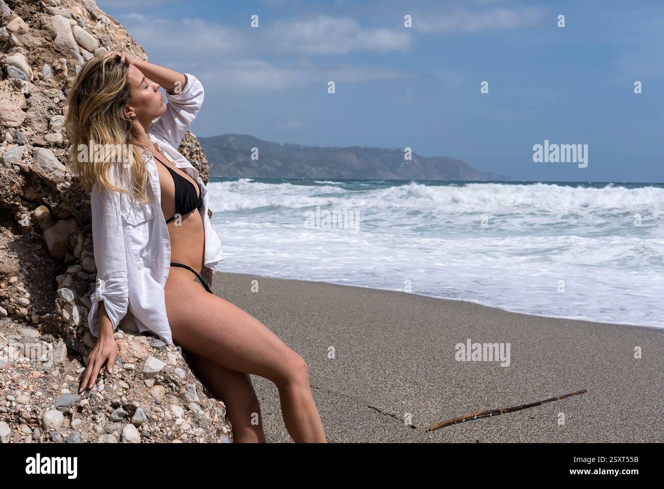 Gorgeous Venezuelan blonde bikini model revels in Alboran Sea's beauty, basking in beach bliss on holiday. Stock Photo
