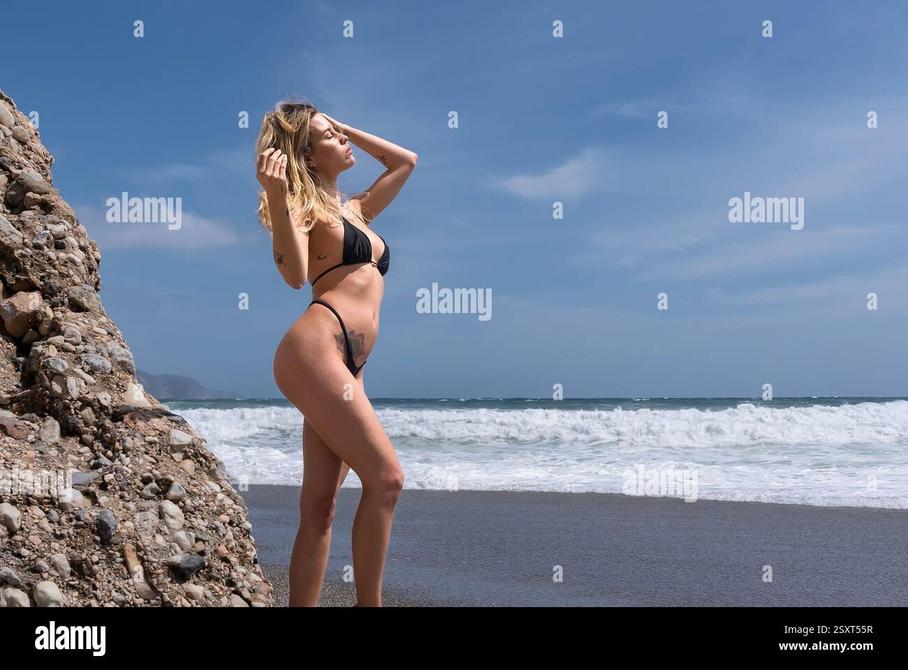 Gorgeous Venezuelan blonde bikini model revels in Alboran Sea's beauty, basking in beach bliss on holiday. Stock Photo