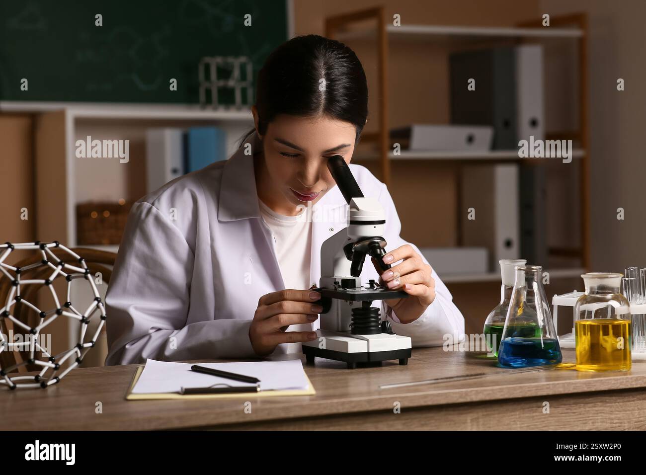 Female inventor looking through microscope at table in laboratory Stock Photo