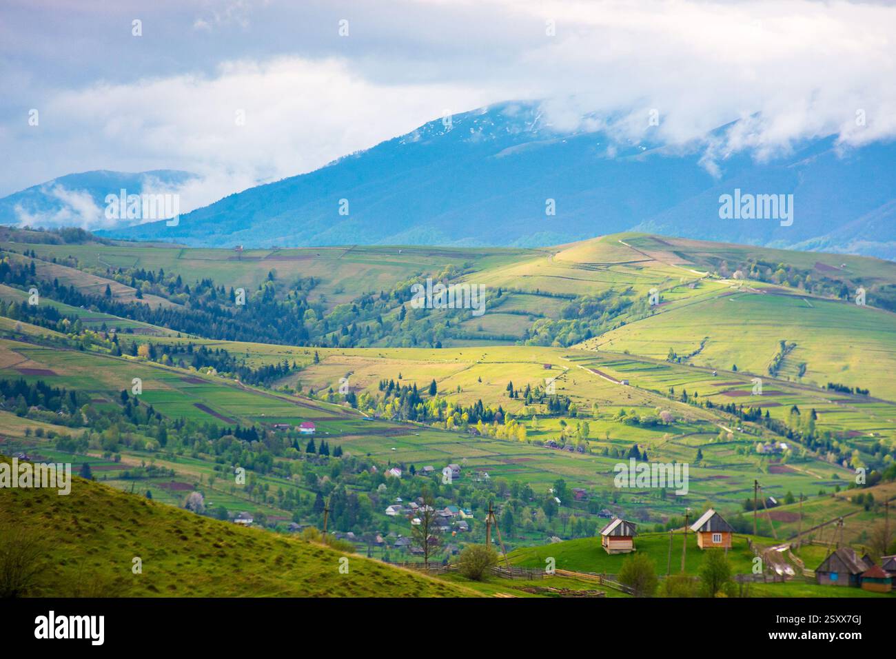 mountainous rural landscape in spring. trees and agricultural fields on hills rolling in to the distant valley. ridge beneath a overcast sky in dapple Stock Photo