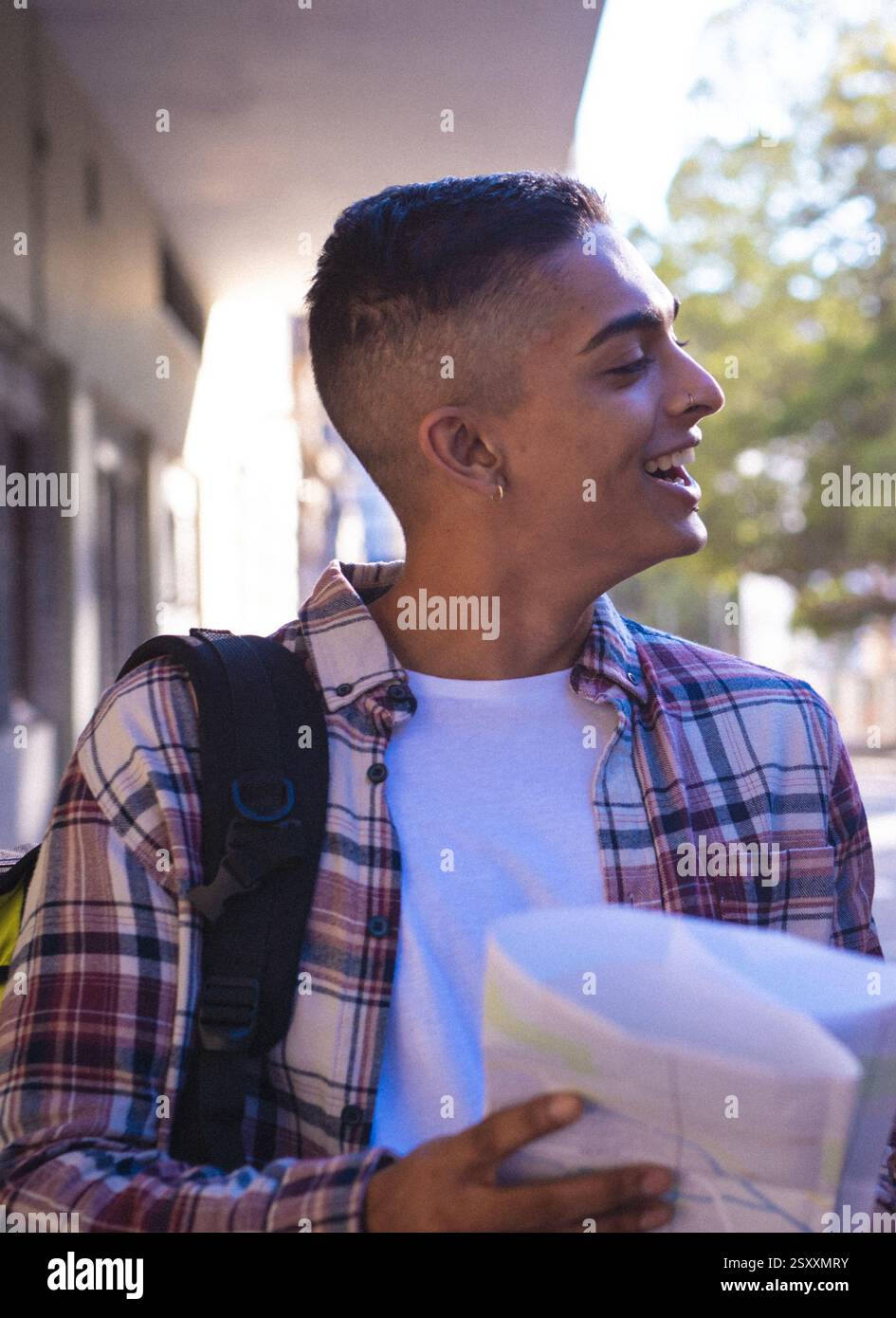 Smiling young man with backpack holding map, exploring city streets Stock Photo
