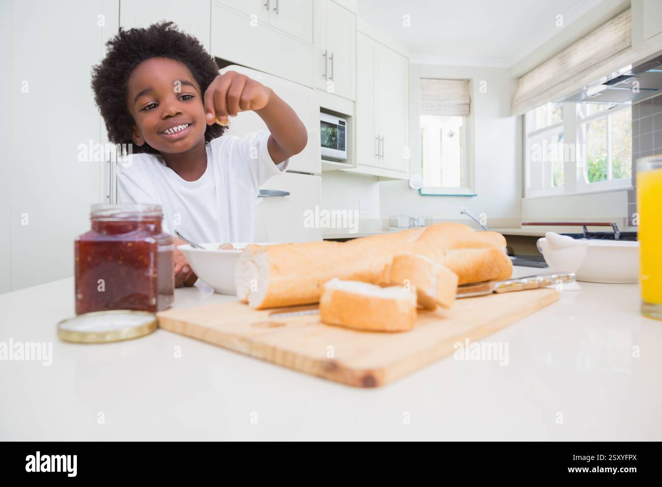 Smiling child enjoying breakfast with bread and jam in bright kitchen Stock Photo