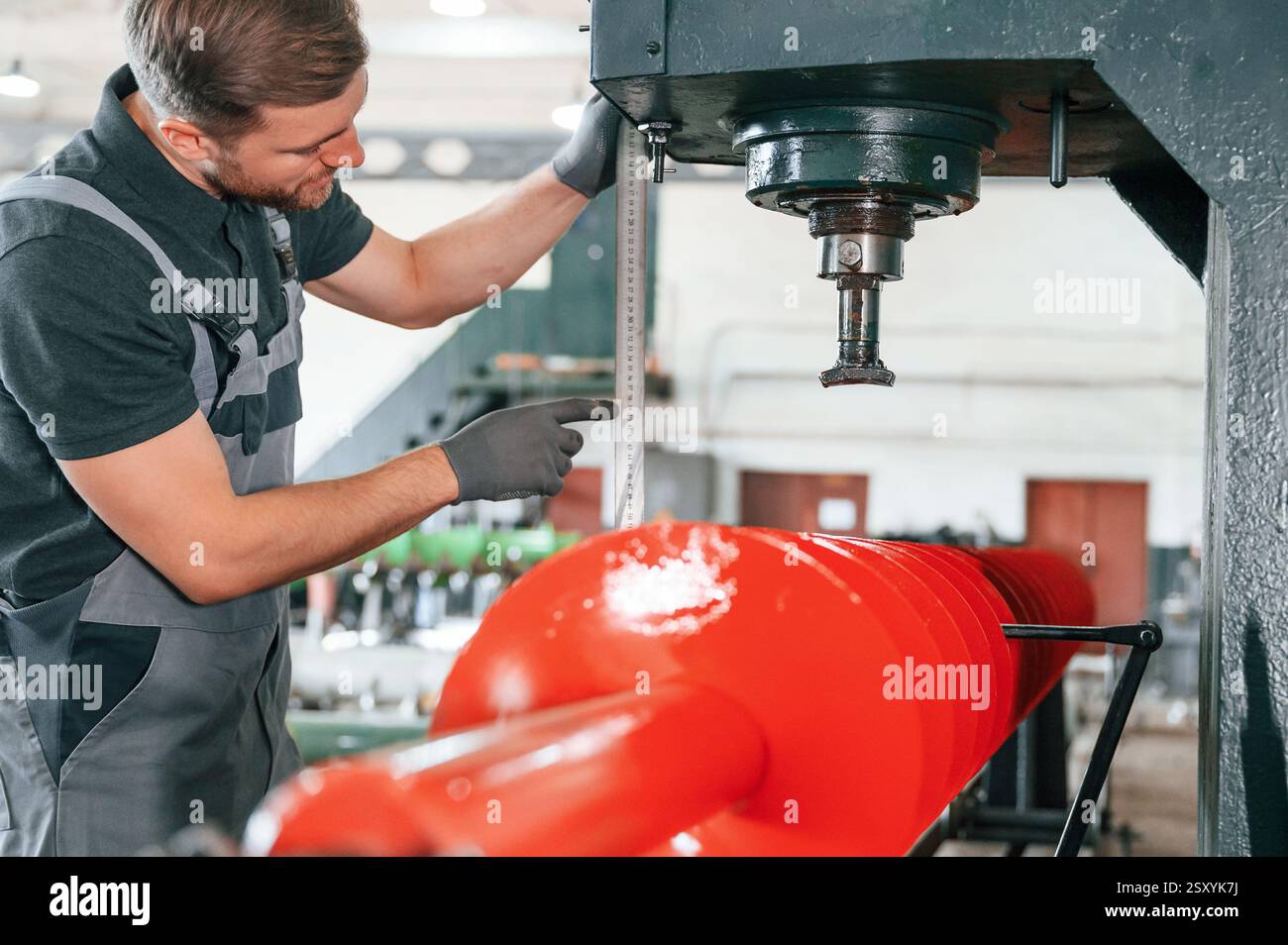 Measuring red colored sharp part. Man in uniform is in workstation developing details of agriculture technique. Stock Photo
