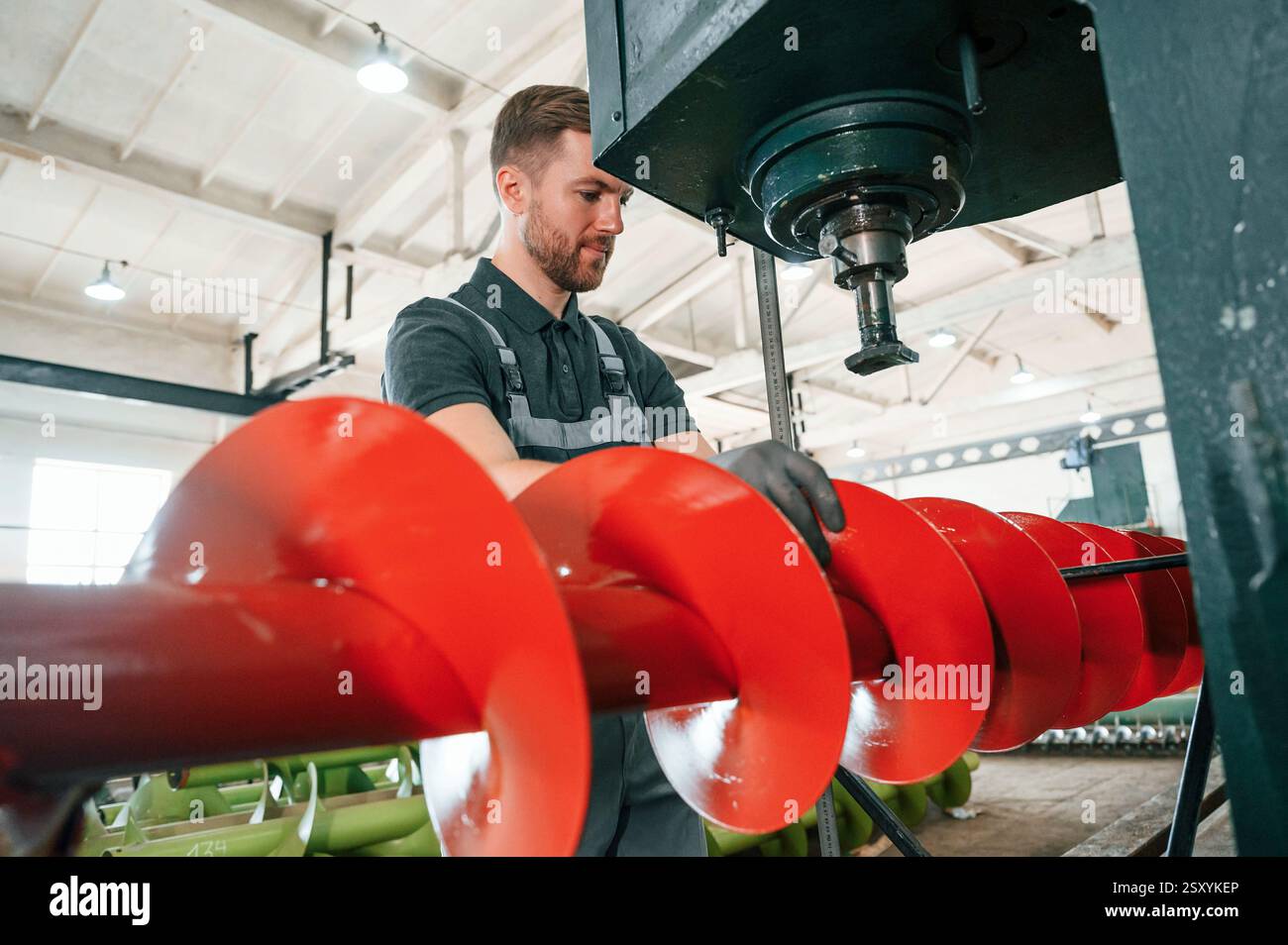 Measuring red colored sharp part. Man in uniform is in workstation developing details of agriculture technique. Stock Photo