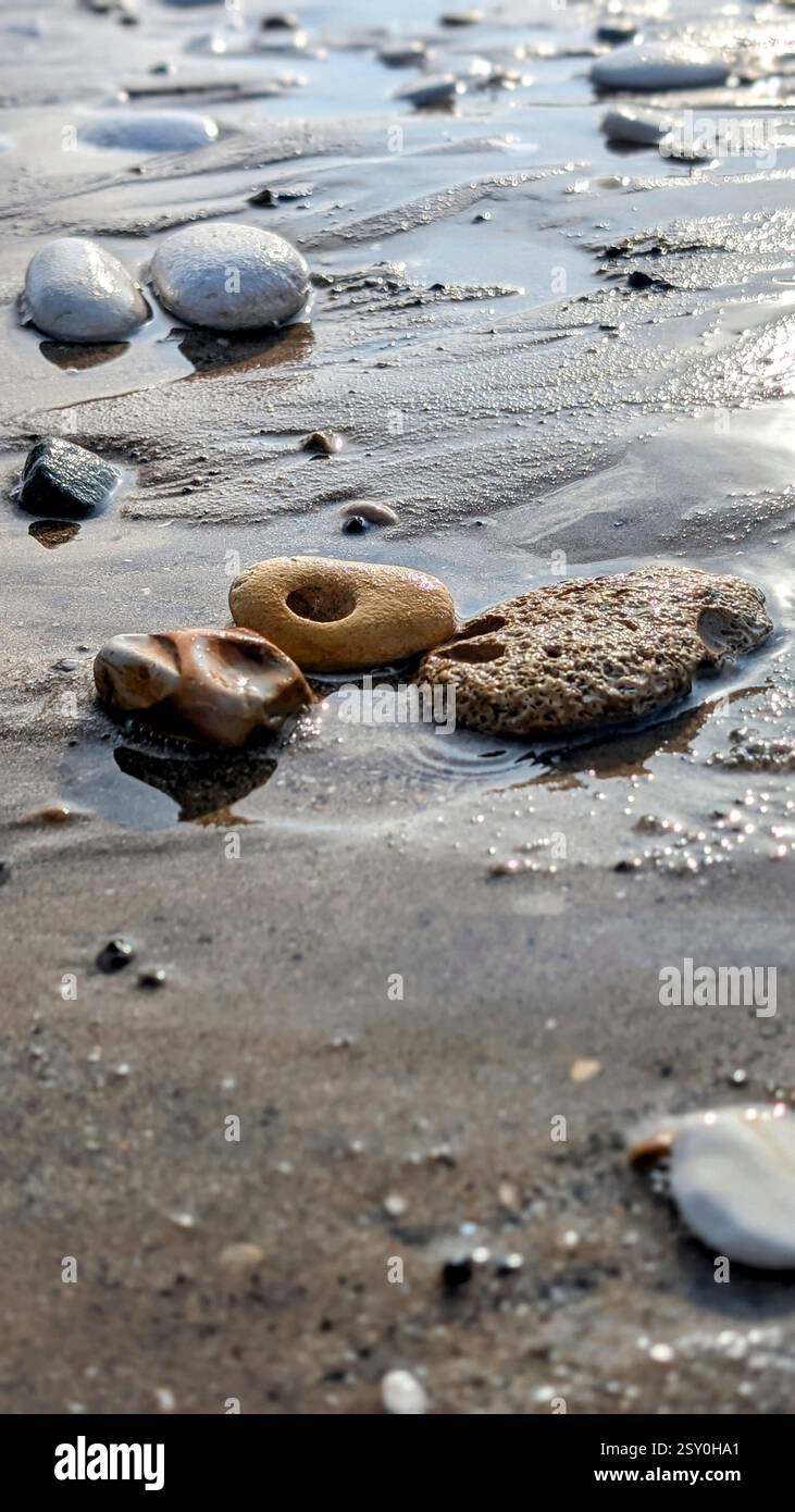 Wet pebbles on sandy beach after tide recedes, showing natural beauty, texture, and reflection in tranquil coastal setting. Ideal for nature projects. - Smartphone Captured Stock Image