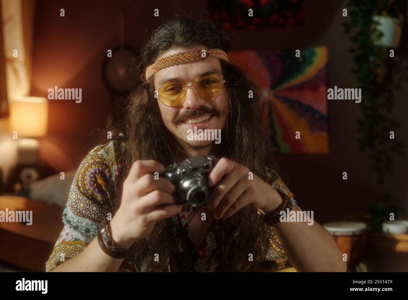 Smiling Man Holding Camera Sitting in Cozy Room Stock Photo