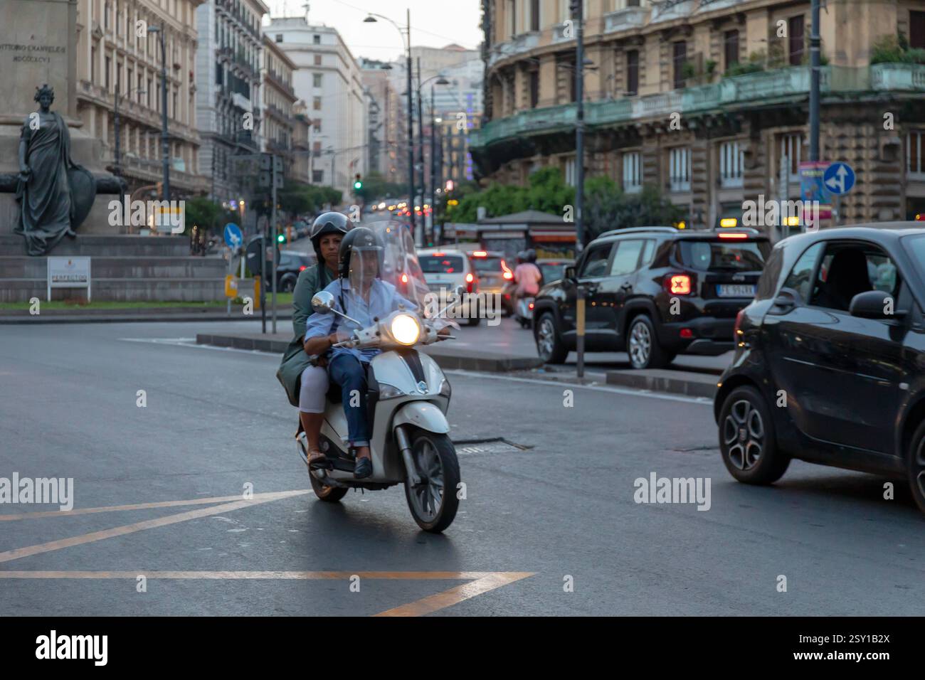 Couple riding a scooter in city traffic. Naples, Italy - June 21, 2019 ...