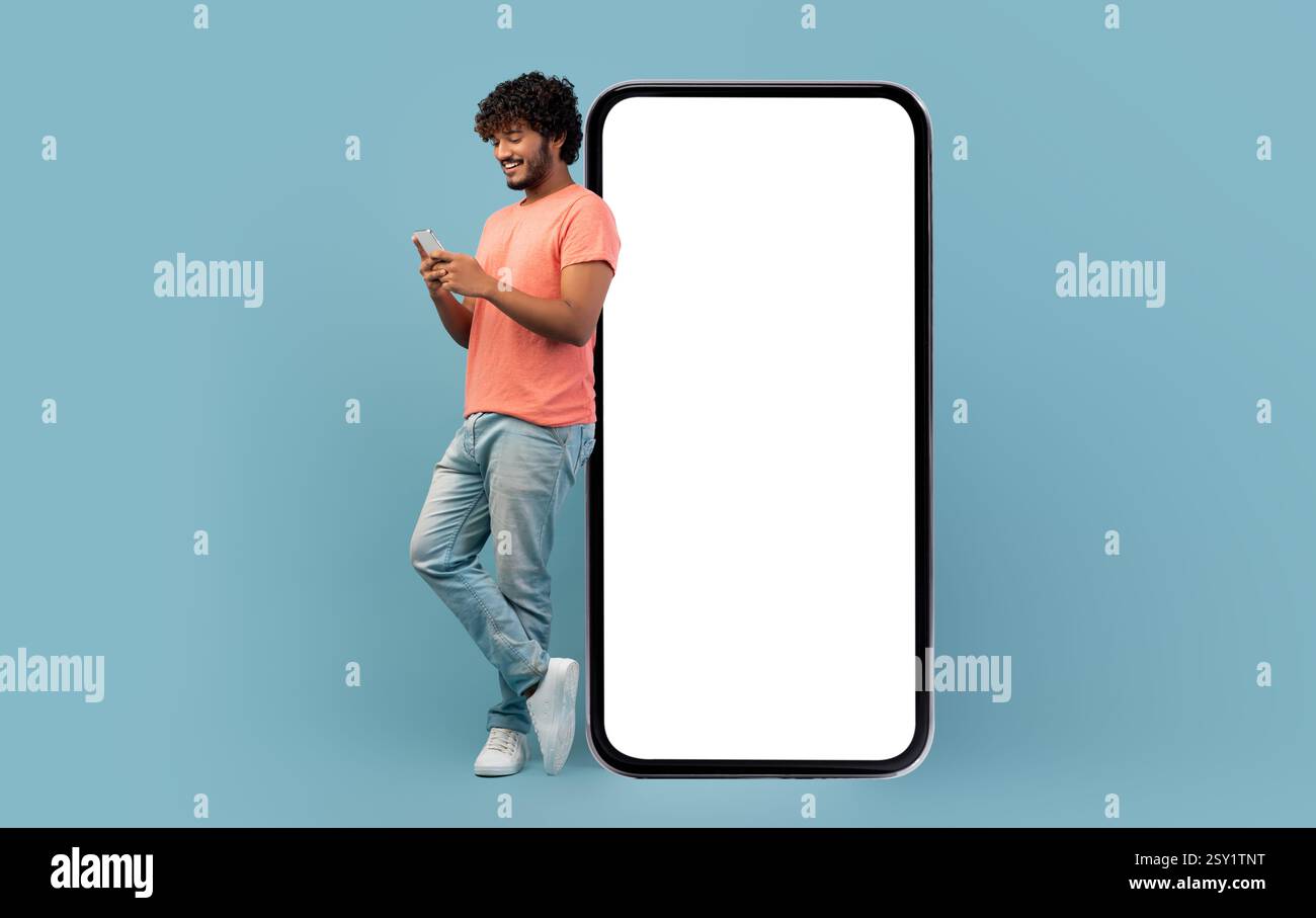 Cool indian guy leaning on huge smartphone, using cell phone Stock Photo