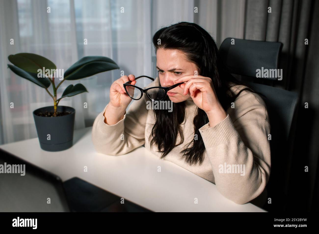 Female with bad eyesight trying to read information from computer using eyeglasses. Freelancer using laptop for work. Stock Photo