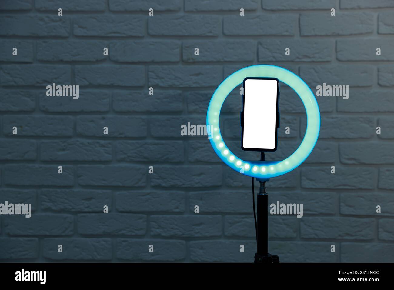 Ring lamp with smartphone against brick wall, space for text Stock Photo