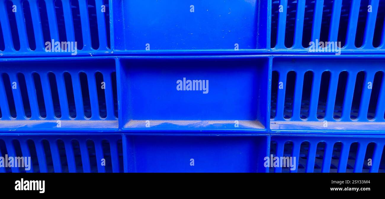 Close up view of a blue plastic crate featuring a grid like pattern with rectangular slits in rows and a solid rectangular section in the center. Stock Photo