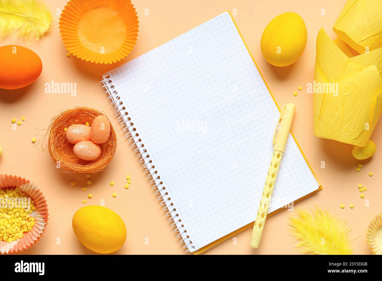 Blank notepad for recipes with pen, Easter eggs and baking molds on orange background Stock Photo