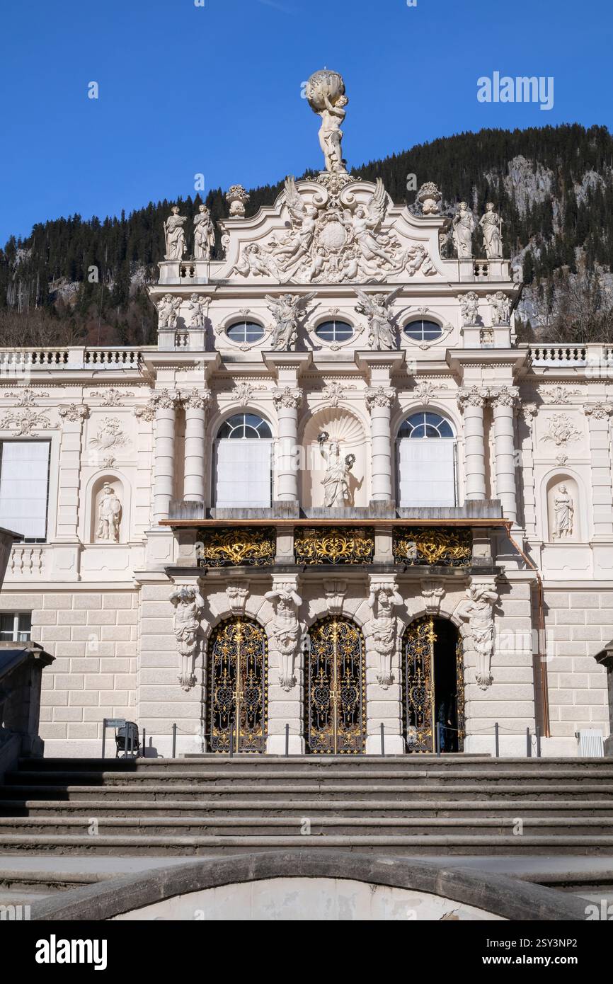 A low-angle, eye-level shot of the Linderhof Palace rooftop, featuring a sculpture of Atlas holding the globe, surrounded by other statues and ornate. Stock Photo