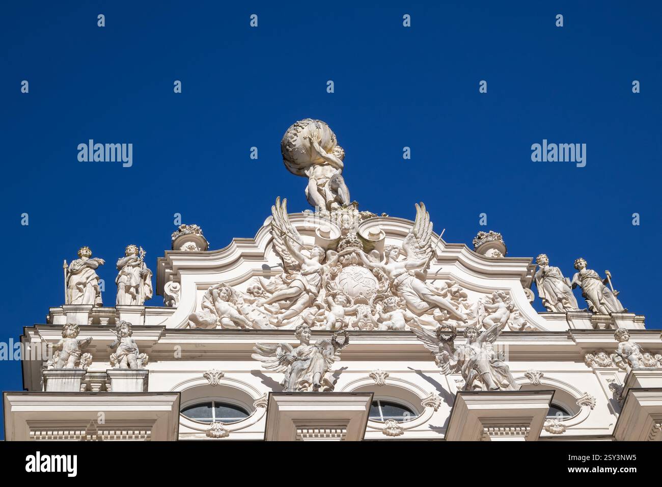 A low-angle, eye-level shot of the Linderhof Palace rooftop, featuring a sculpture of Atlas holding the globe, surrounded by other statues and ornate. Stock Photo