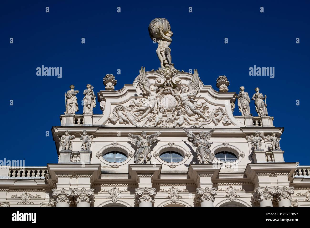 A low-angle, eye-level shot of the Linderhof Palace rooftop, featuring a sculpture of Atlas holding the globe, surrounded by other statues and ornate. Stock Photo