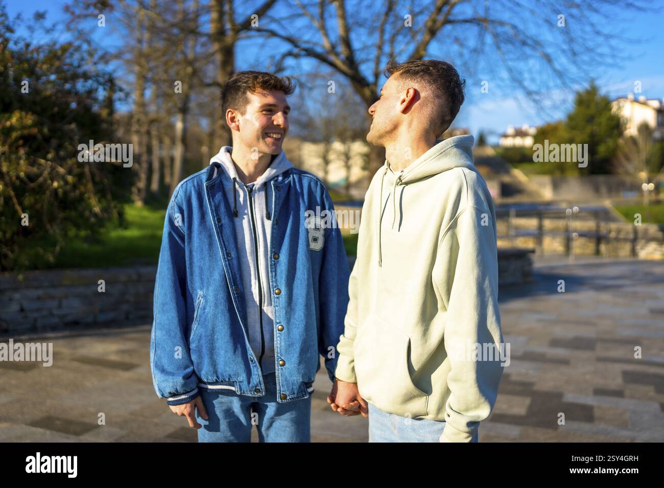 Two young men holding hands and smiling at each other while walking in ...