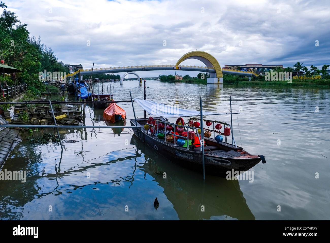 An excursion boat moored on the Thu Bon River, Sông Thu Bồn, the Moonlight Bridge, Ành trâng in the distance. Stock Photo