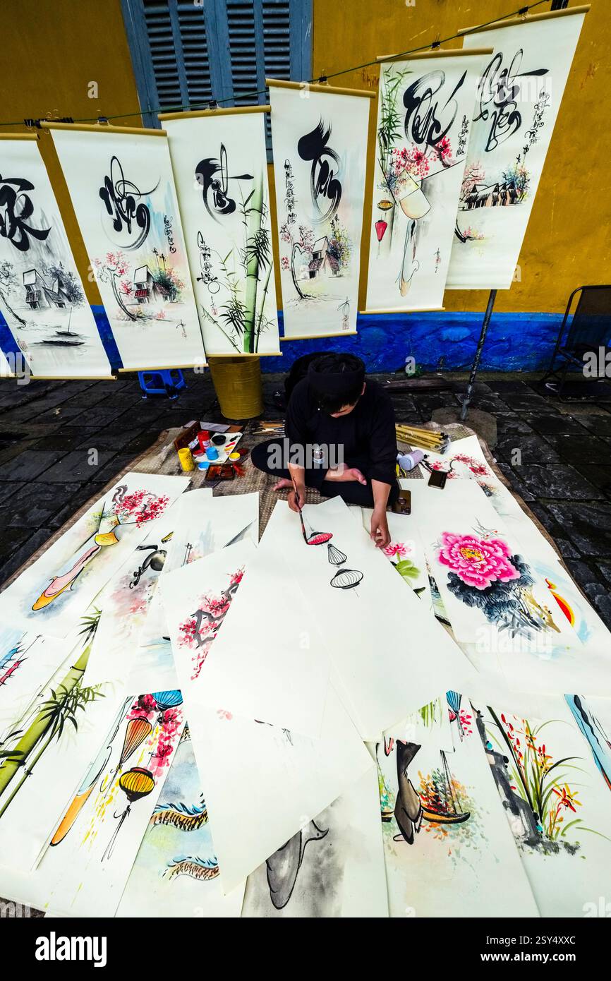 An artist paints colourful pictures with ancient Chinese characters on a footpath in Hoi An, Hái An. Hoi An Quang Nam Province Vietnam FB 2024 4232 Stock Photo