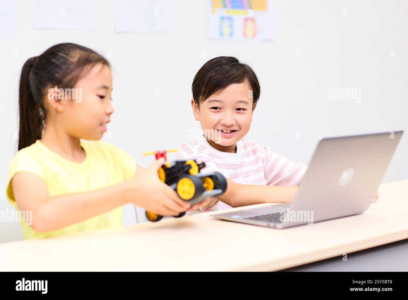 Two Children Sitting At A Table With A Laptop Stock Photo