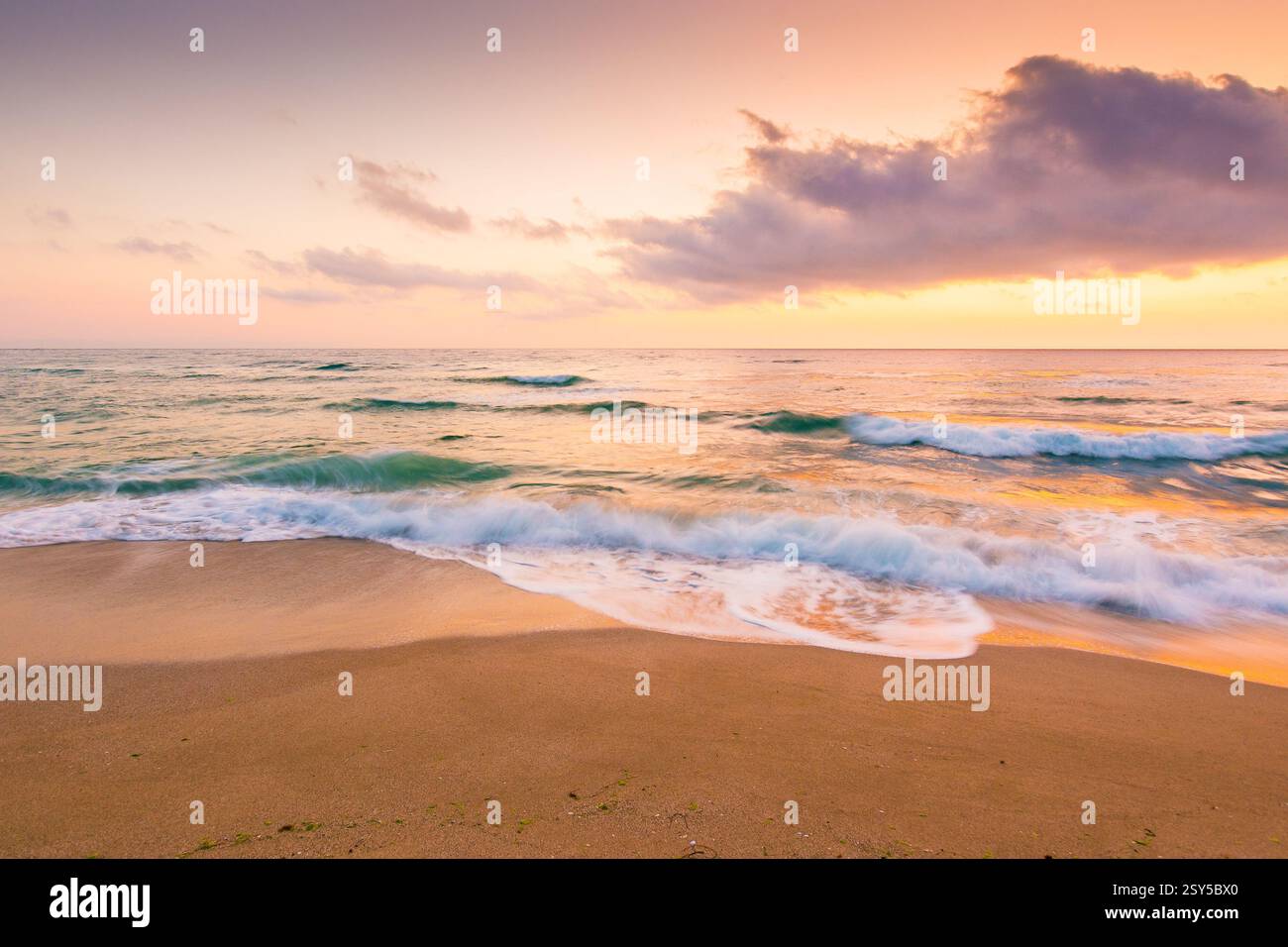 summer vacation at the sea. outdoor adventure. beautiful purple pink seascape at sunrise. calm waves wash the golden sandy beach. fluffy clouds on the Stock Photo