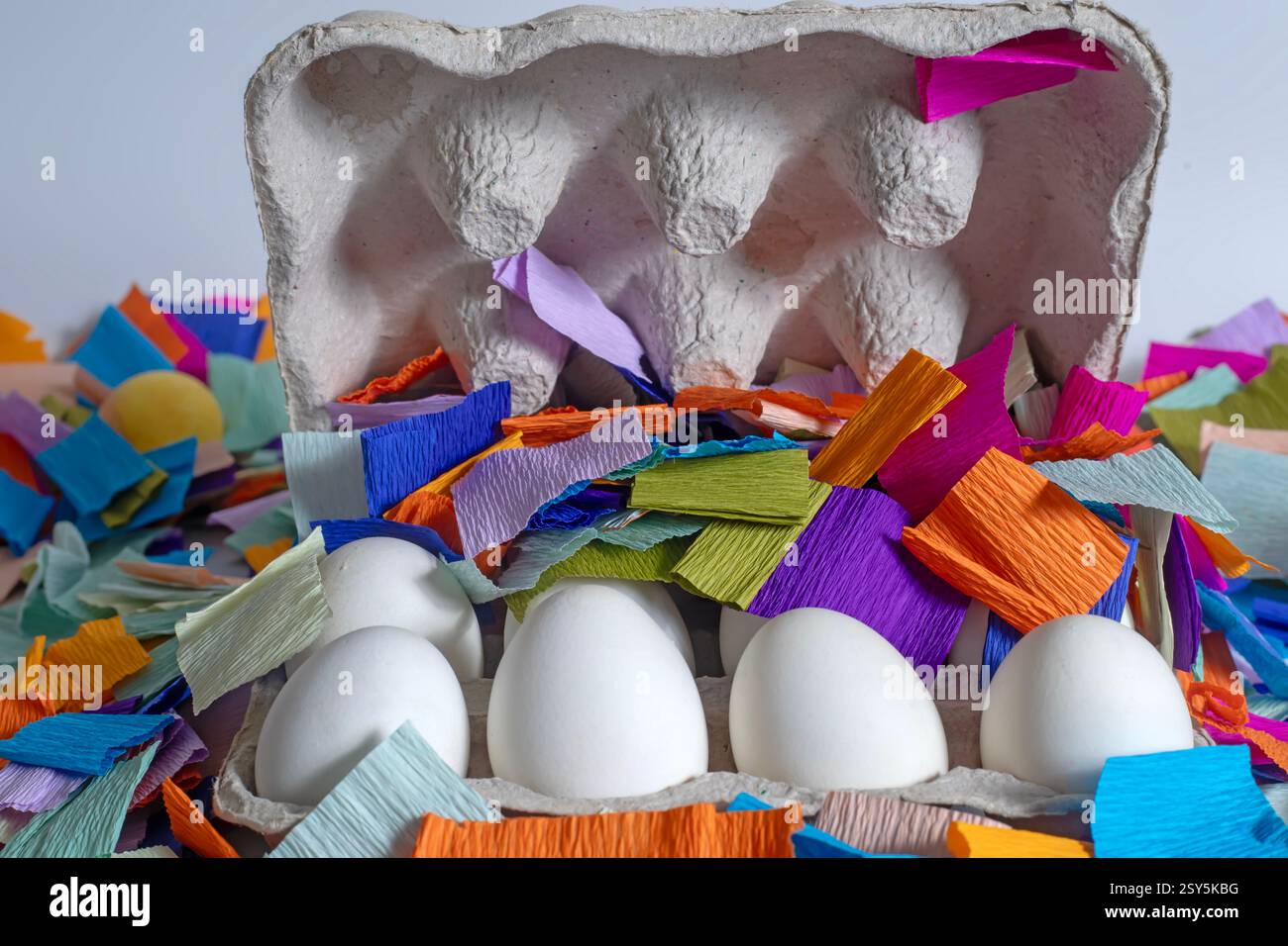 Brightly colored paper pieces scattered around white eggs in a cardboard box. Perfect for celebrations, festive marketing materials. Stock Photo