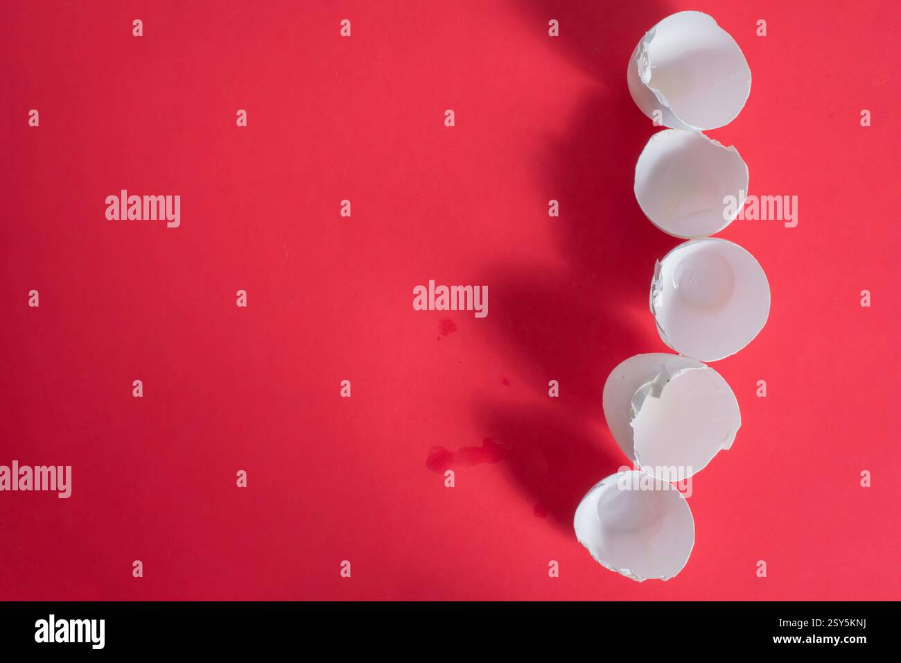 Five broken eggshells artistically placed on a red surface, creating an abstract and minimalist composition. Stock Photo