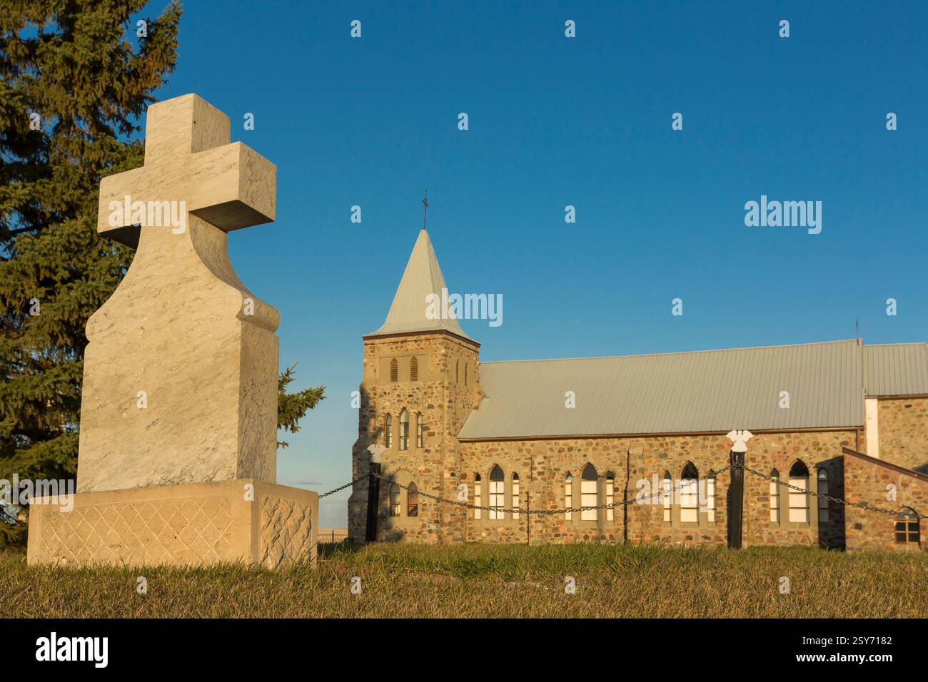 Large stone cross is in front of a church. The cross is on a hill and the church is on a hill as well Stock Photo
