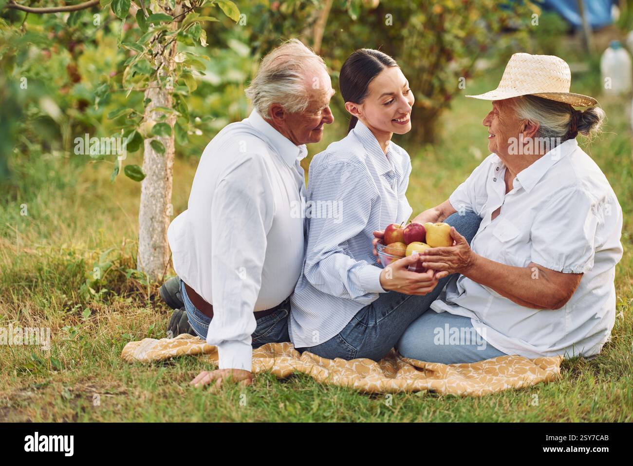 With apples. Sitting on the ground. Daughter is with her senior mother and father is in the garden. Stock Photo