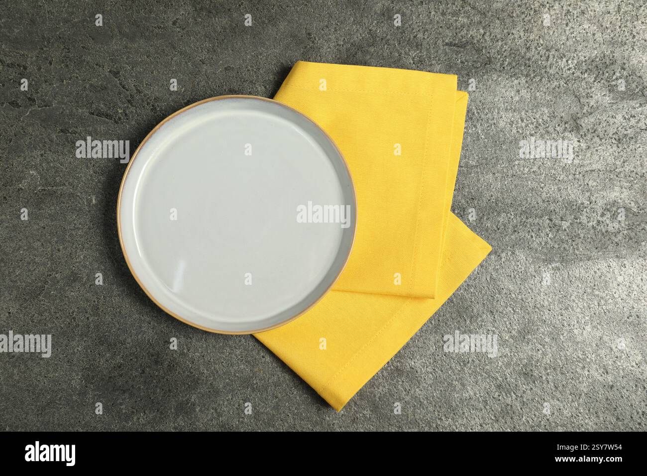 Yellow napkin and empty plate on grey table, top view Stock Photo