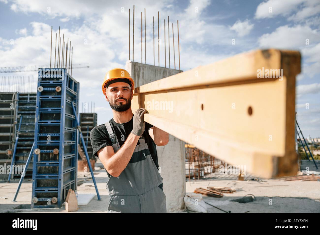 Carrying wooden plank. Man in uniform is working on the construction site. Stock Photo