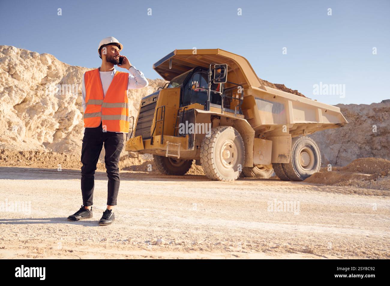 Using smartphone. Man in uniform is working in the quarry at daytime. Stock Photo