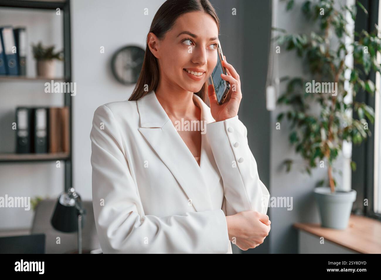 Talking by phone. Young beautiful woman in formal clothes is working at office. Stock Photo