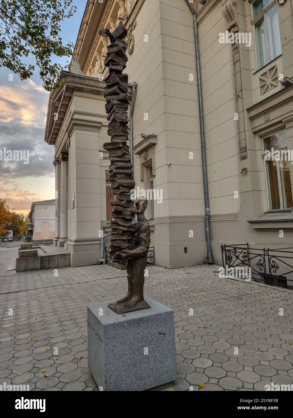 Reader statue: artwork, sculpture of a person carrying a large high pile of books, in front of the Odesa National Scientific Library in Odesa (Odessa) - Smartphone Captured Stock Image