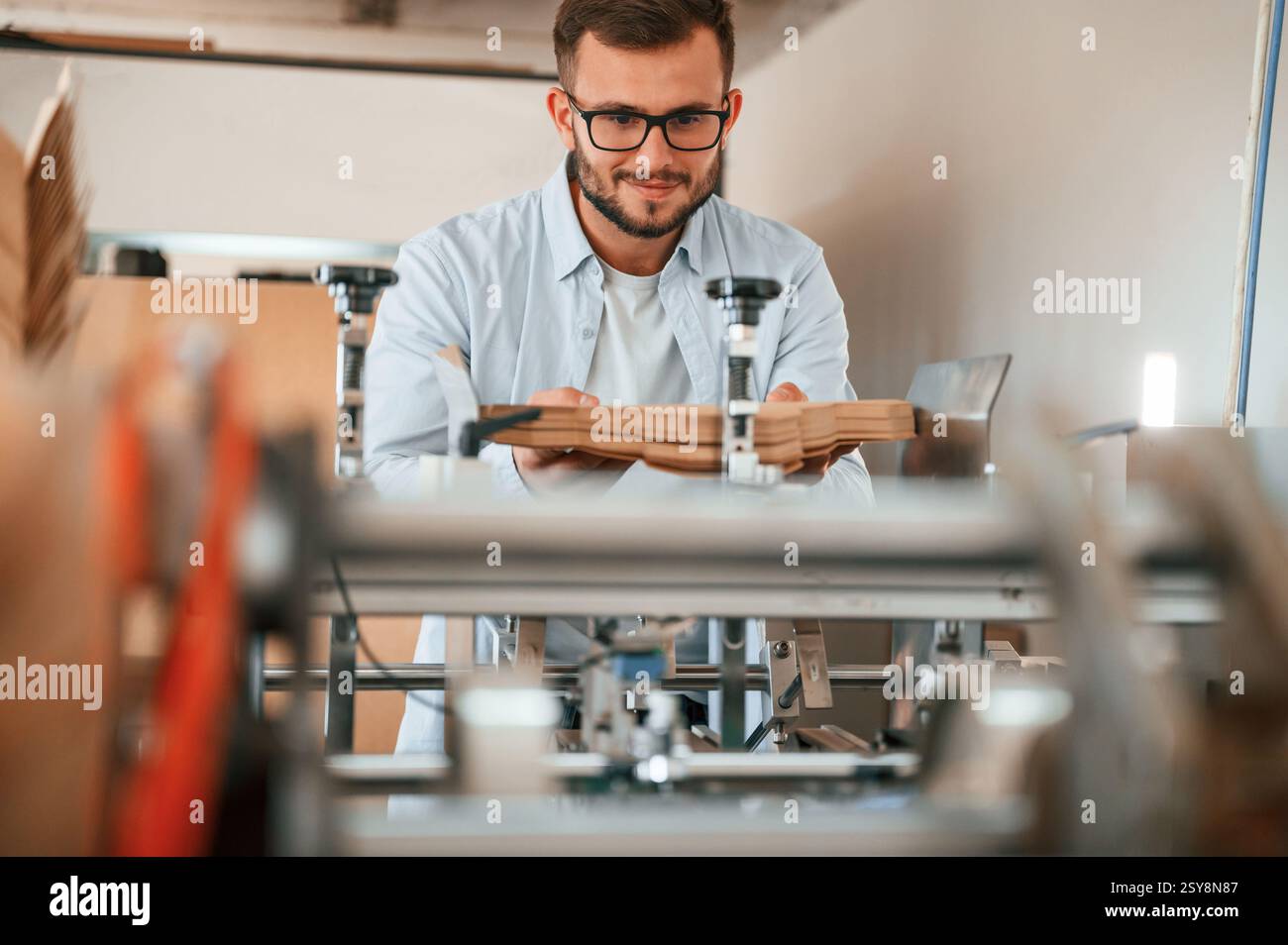 Using the cutting machine. Print house worker in white clothes is indoors. Stock Photo