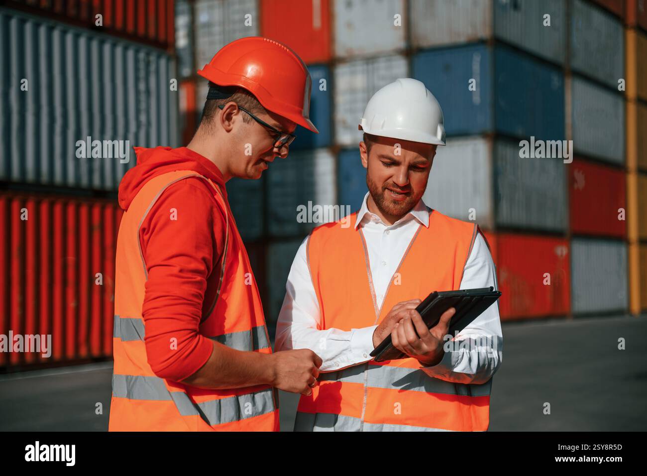 Using digital tablet. Two male workers is on the location with containers. Stock Photo