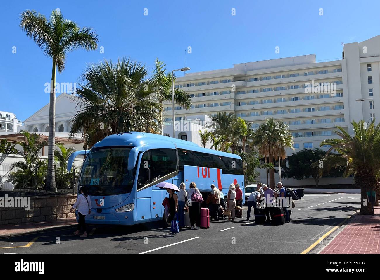 Passengers standing beside a TUI Transfer Bus as their suitcases are loaded onboard. Costa Adeje, Tenerife, Canary Islands, Spain. 28th January 2025. - Smartphone Captured Stock Image
